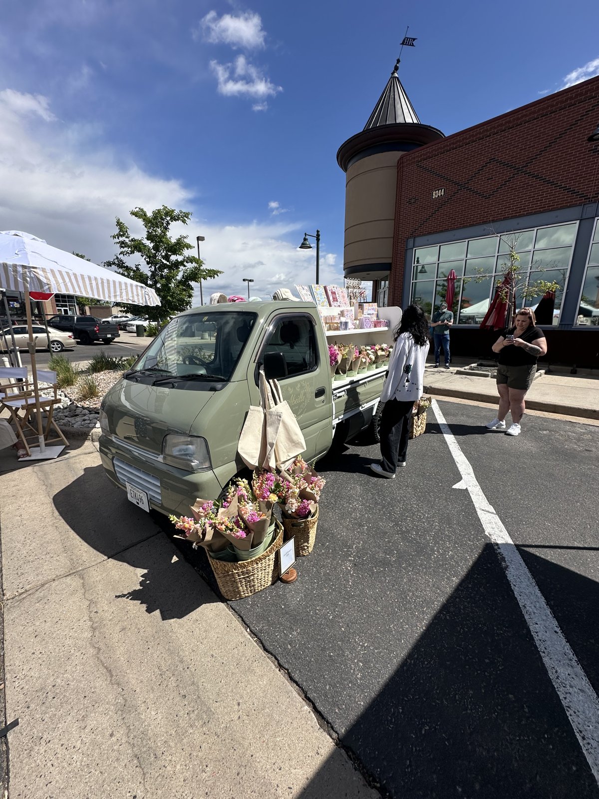 A renovated mini-truck loaded with fresh pink and yellow bouquets parked at the Highlands Ranch Farmers Market at Town Center on 5/17/2026